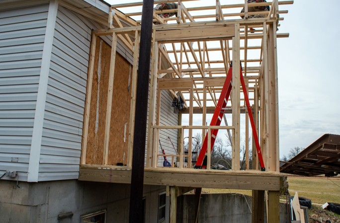 Wooden framing of a house extension under construction, attached to an existing white-sided building.